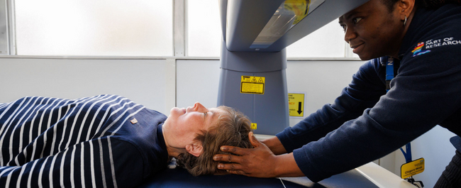 Photo of a lady lying on a DXA scanner supported by a fieldworker 